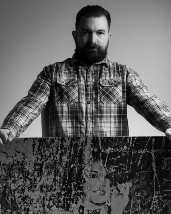 Foto de um homem com barba segurando uma obra de arte