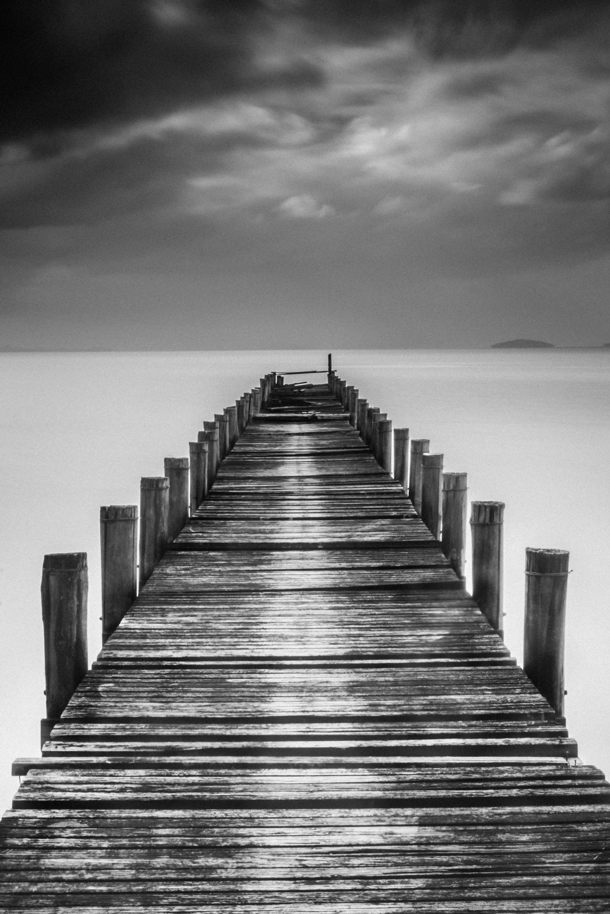Imagem em preto e branco de uma ponte de madeira sobre um rio que parece nuvem | Adriano Bassegio